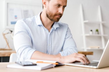 Ofiste masasında otururken dizüstü bilgisayar üzerinde çalışan ciddi işadamı kırpılmış görüntü