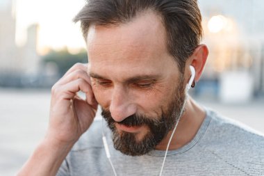 İmge-in yakışıklı güçlü olgun sporcu ayakta açık havada bir kenara dinleme müzik kulaklık arıyorum.