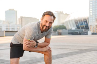 Yakışıklı mutlu güçlü olgun sporcu ayakta açık havada kamera seyir görüntüsünü.