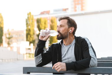 Açık havada su şişesiyle içme kulaklık ile bir kenara dinleme müzik arıyorum yakışıklı güçlü olgun sporcu görüntüsünü.