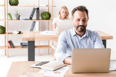 Bir arka plan ile işbirliği işçisi kadın ofiste otururken dizüstü bilgisayarda çalışarak gülümseyen adam Yöneticisi