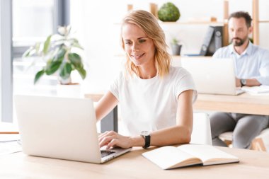 Bir arka plan üzerinde adam işbirliği işçi ile ofiste otururken dizüstü bilgisayarda çalışarak gülümseyen kadın Yöneticisi