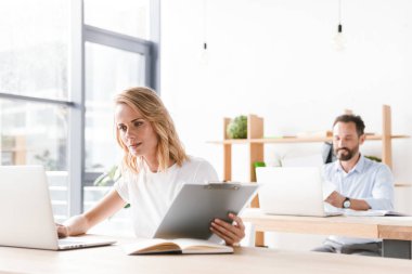 Bir arka plan üzerinde adam işbirliği işçi ile ofiste otururken dizüstü bilgisayar belgelerle çalışma odaklı kadın Yöneticisi