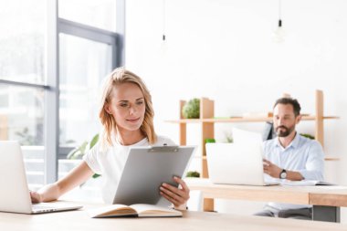 Güzel kadın Yöneticisi ofiste adam işbirliği işçi ile bir arka plan üzerinde otururken dizüstü bilgisayar belgelerle çalışma