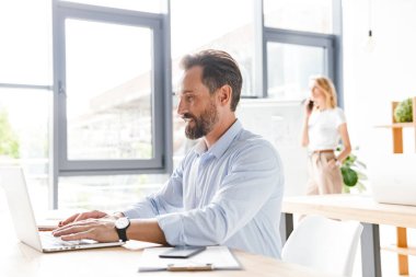 Bir arka plan ile işbirliği işçisi kadın ofiste otururken dizüstü bilgisayar ve belgeler üzerinde çalışan gülümseyen adam Yöneticisi