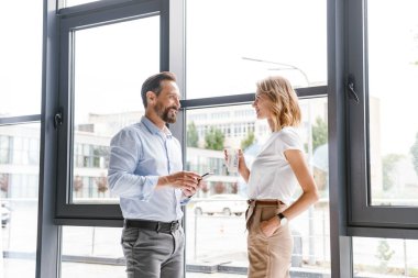 Cep telefonu ve fincan kahve ile office pencerede dururken konuşmaya gülümseyen iş arkadaşları birkaç
