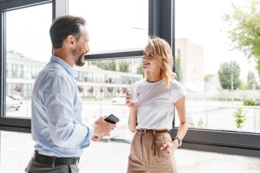 Çift mutlu meslektaşlarının duran cep telefonu ve fincan kahve ile ofis pencerenin konuşuyor