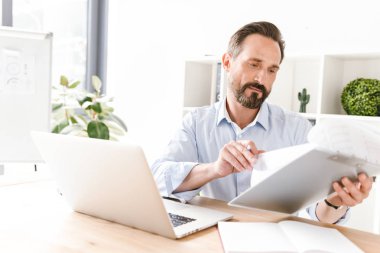 İşadamı holding klasör evrak ve dizüstü bilgisayar ile ofis masa başında otururken gülümseyen