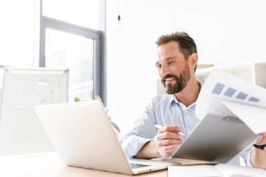 Klasör evrak ve dizüstü bilgisayar ile ofis masa başında otururken holding neşeli işadamı