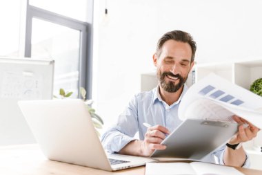 Mutlu işadamı klasör evrak ve dizüstü bilgisayar ile ofis masa başında otururken holding