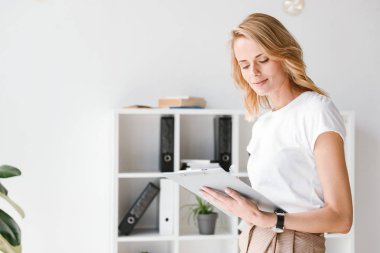 Akıllı işkadını bir ofis masa üzerine eğilerek belgeleri analiz etme