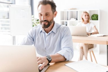 Çekici bir adam Yöneticisi bir arka plan ile işbirliği işçisi kadın ofiste otururken dizüstü bilgisayar ve belgeler üzerinde çalışma