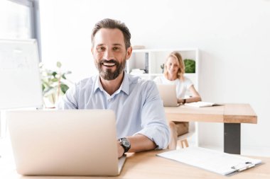 Bir arka plan ile işbirliği işçisi kadın ofiste otururken dizüstü bilgisayar ve belgeler üzerinde çalışan gülen adam Yöneticisi