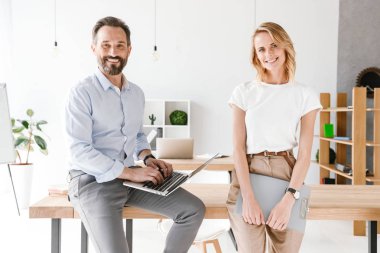 Adam Yöneticisi holding laptop evrak ile ayakta işbirliği işçisi kadın ile ofiste bir masa üzerine eğilerek süre gülümseyen