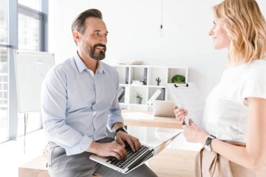 Dizüstü bilgisayar ile evrak ile ayakta işbirliği işçisi kadın ofiste bir masa üzerine eğilerek süre tutarak samimi adam Yöneticisi