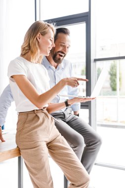 Memnun meslektaş ofis pencerenin önünde duran ve parmak işaret ederken dizüstü bilgisayar üzerinde çalışan birkaç