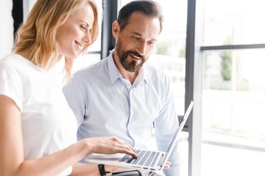 Çift ofis pencerenin önünde duran dizüstü bilgisayar üzerinde çalışan genç meslektaşlarının