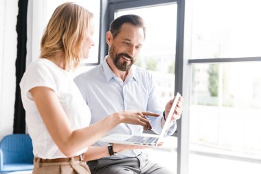 Çift ofis pencerenin önünde duran ve parmak işaret ederken dizüstü bilgisayar üzerinde çalışan genç meslektaşlarının