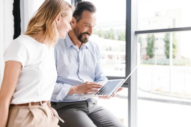 Birkaç heyecanlı meslektaş ofis pencerenin önünde duran dizüstü bilgisayar üzerinde çalışan