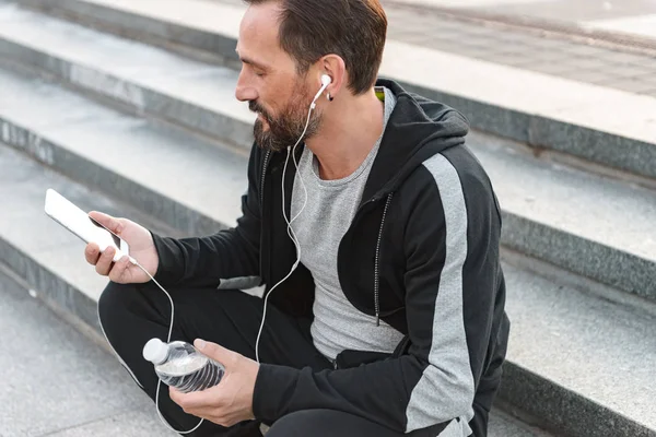 Fokuserade Sportsman Hörlurar Använder Mobiltelefon Medan Sitter Steg Med Vattenflaska — Stockfoto