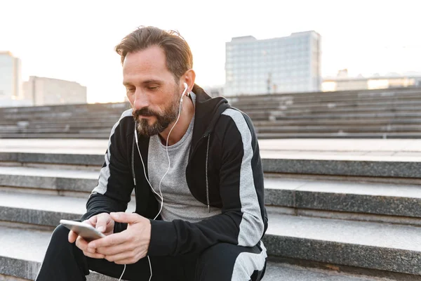 Guapo Deportista Auriculares Sosteniendo Teléfono Móvil Mientras Está Sentado Los — Foto de Stock