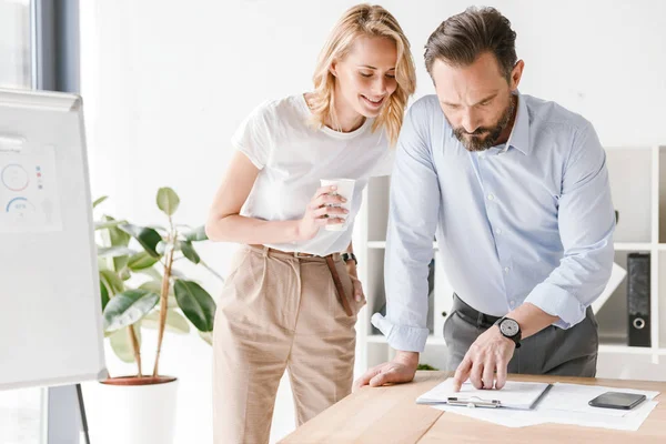 Ofiste ayakta ve Yönetim Kurulu ve belgeleri çalışma sırasında iş tartışırken gülümseyen iş arkadaşları birkaç proje