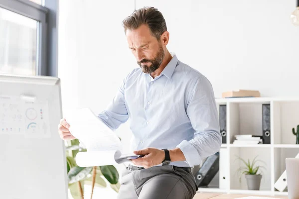 Hombre Negocios Concentrado Analizando Papeleo Mientras Apoya Escritorio Oficina — Foto de Stock