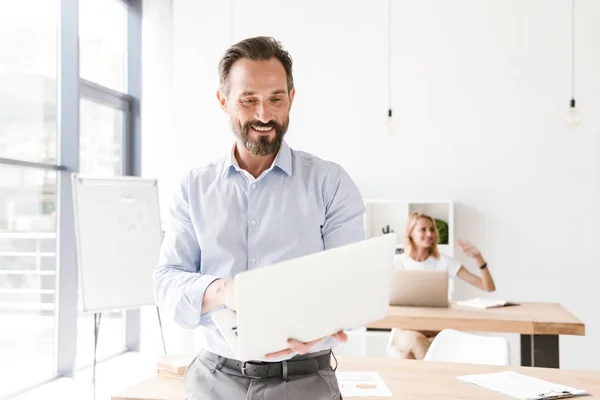 Усміхнений Менеджер Чоловіка Тримає Ноутбук Спираючись Стіл Офісі Жінкою Співробітницею — стокове фото
