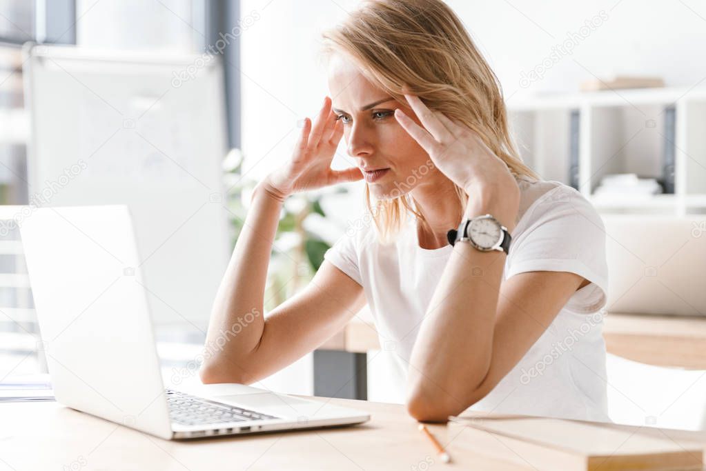 Tired businesswoman working on laptop computer while sitting at the office desk