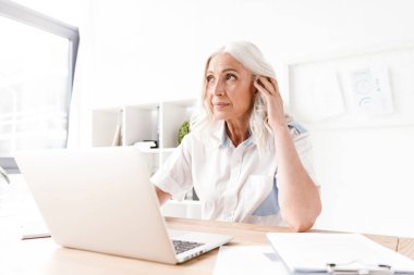 Kapalı dizüstü bilgisayar ile çalışma ofisinde oturan konsantre Olgun kadın görüntüsünü.