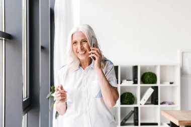 Kapalı cep telefonu ile konuşurken office çalışan olgun mutlu kadın fotoğrafı.