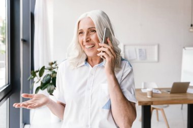 Kapalı cep telefonu ile konuşurken office çalışan olgun mutlu kadın fotoğrafı.