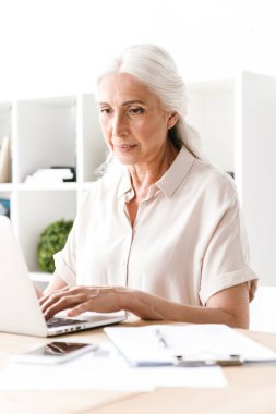 Ofiste masasında otururken dizüstü bilgisayar üzerinde çalışan emin olgun iş kadın