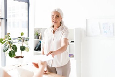 Olgun busienss kadın alarak belgeler Office masasında duran gülümseyen