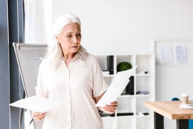 Emin olgun iş kadını ofiste dururken belgeleri analiz etme