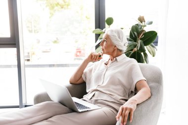 İçeride koltukta otururken dizüstü bilgisayar üzerinde çalışan dalgın olgun iş kadın