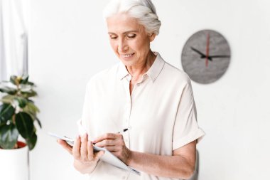 Gülümseyen olgun iş kadını ofiste dururken not alma