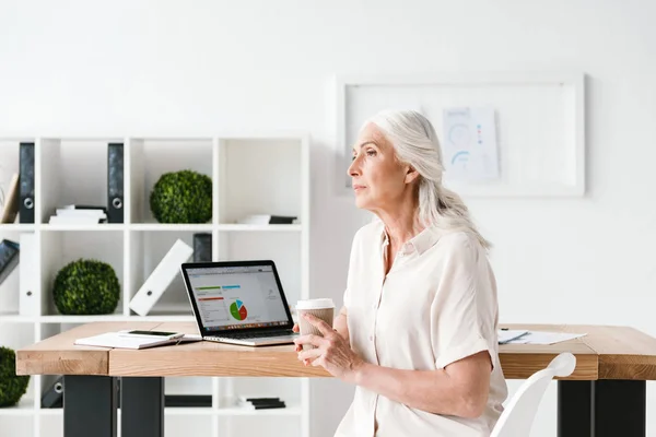 成熟したビジネスの成功女性ラップトップ コンピューターに取り組んで オフィスで机に座ってコーヒーを飲みながら — ストック写真