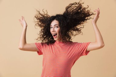 Görüntü şirin mutlu genç kadının saçını sallayarak bej duvar arka plan üzerinde izole ayakta.