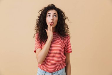 Bir kenara seyir bej duvar arka plan üzerinde izole duran sevimli şok genç kadın görüntüsünü.