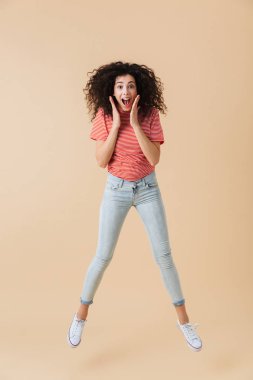 Görüntü izole kamera seyir bej duvar arka plan üzerinde atlama şok genç ve güzel kadın.