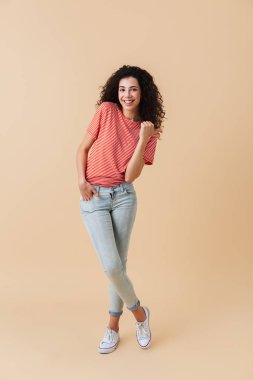 Esmer kıvırcık saçlı kopya alanı işaret mutlu bir genç kadın portresi tam uzunlukta bej renkli arka plan üzerinde izole