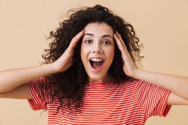 Bej renkli arka plan üzerinde izole duran şok genç kıvırcık kadın görüntüsü. Görünümlü kamera.