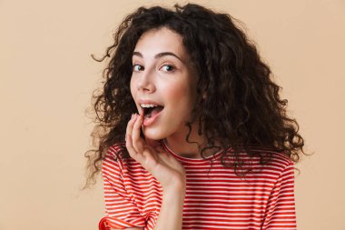 Bej renkli arka plan üzerinde izole duran sevimli güzel genç kıvırcık kadın fotoğrafı. Görünümlü kamera.