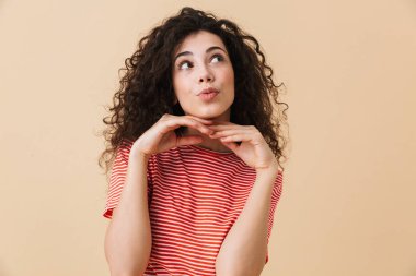 Tatlı rüya genç kıvırcık kadın bej renkli arka plan üzerinde izole ayakta fotoğrafı.