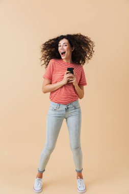 Cep telefonu bej renkli arka plan üzerinde izole holding neşeli bir casual kız portresi tam uzunlukta