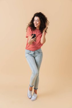 Bej renkli arka plan üzerinde izole cep telefonunuzla bir selfie alarak mutlu bir casual kız portresi tam uzunlukta