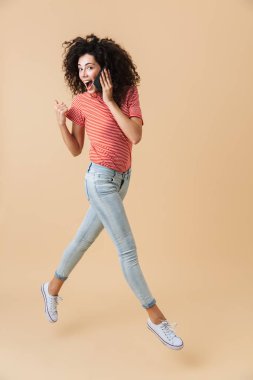 Tam uzunlukta portre heyecanlı bir genç kızın cep telefonu çalıştıran ve uzak işaret bej renkli arka plan üzerinde izole süre konuşuyor