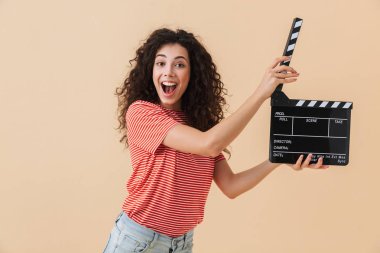 Sevimli Genç ve güzel kıvırcık kadın Klaket yapım film tutan bej renkli arka plan üzerinde izole görüntüsünü.