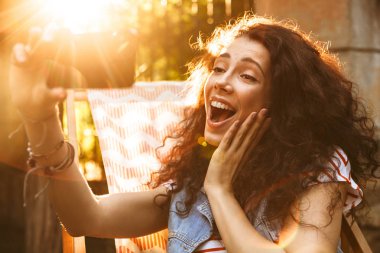 Güneşli günde 18-20 bağırarak ve sırasında selfie fotoğraf çekerken cep telefonu arıyorum şezlong Park içinde dinlenme şirin neşeli kadın portresi